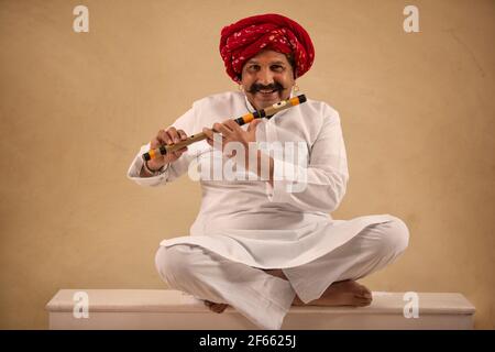 A HAPPY TURBANED MAN SITTING WITH HIS FLUTE TO PLAY Stock Photo