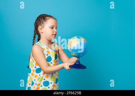 portrait of girl in white summer dress with colorful circles rotating a globe in her hands and dreaming of a vacation, isolated on a blue background Stock Photo