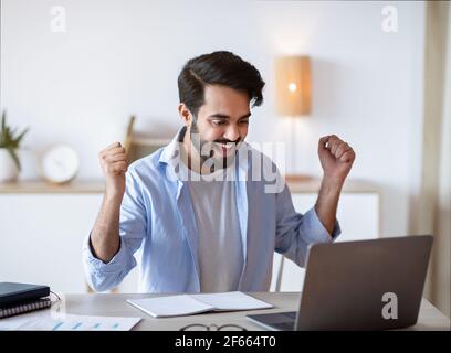 Promotion News. Overjoyed Arab Man Looking At Laptop Screen And Celebrating Success Stock Photo