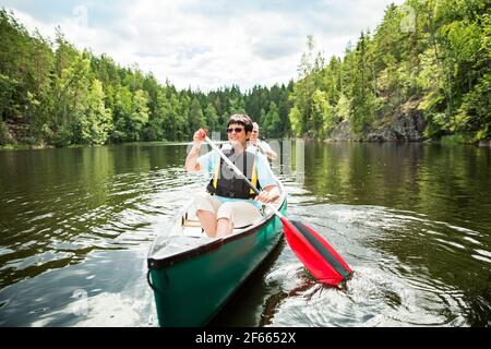 Happy mature couple in life vests canoeing in forest lake. Sunny summer day. Tourists traveling in Finland, having adventure. Stock Photo