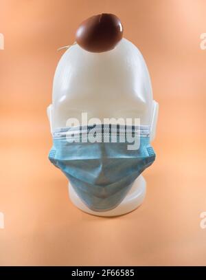 Abstract modern composition, human face with a mask, Easter egg falling on a head. Minimalist abstract composition background of a human masked face. Stock Photo