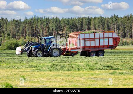 Collecting cut hay for silage with Pöttinger Europrofi 3 silage trailer pulled by a New Holland tractor on a day of summer. Salo, Finland. July 26, 20 Stock Photo