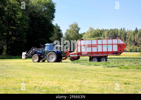 Collecting hay for silage with Pöttinger Europrofi 3 silage trailer pulled by a New Holland tractor on a day of summer. Salo, Finland. July 26, 2020. Stock Photo
