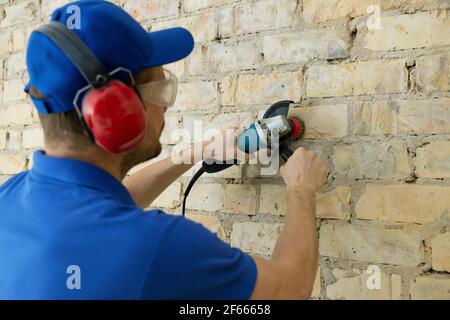 worker cleaning old brick wall with rotary wire brush Stock Photo