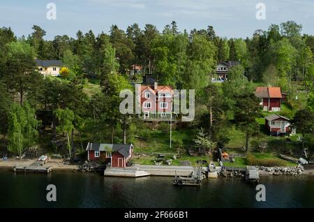 Colourful wooden buildings by the waterfront (Baltic Sea), trees behind, in the Aland Islands, Finland. Stock Photo