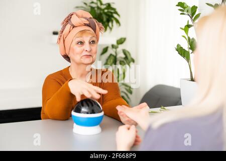 Female Fortuneteller or esoteric Oracle, sees in the future by looking into their crystal ball during a Seance to interpret them and to answer Stock Photo