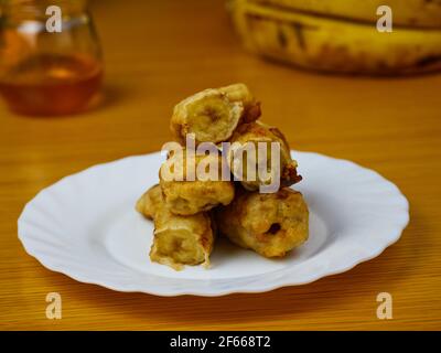 Fried slices of the ripe plantain on a white dish decorated with bananas and honey Stock Photo