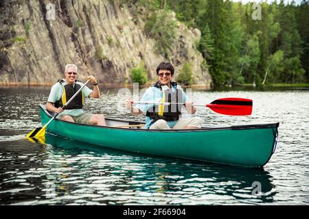Happy mature couple in life vests canoeing in forest lake. Sunny summer day. Tourists traveling in Finland, having adventure. Stock Photo