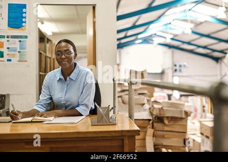 Smiling young African woman working at her desk in a warehouse Stock Photo
