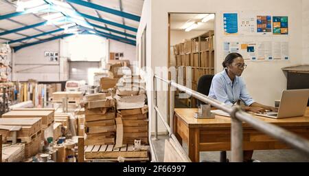 Young African woman using a laptop at her warehouse desk Stock Photo