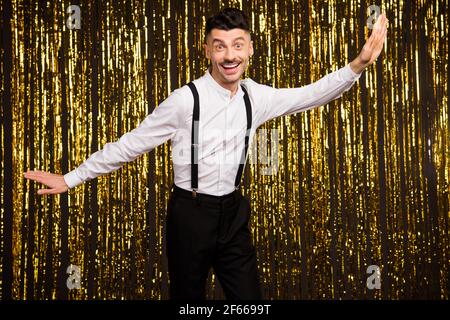 Photo of pretty funny young man wear white shirt smiling arms sides dancing isolated golden glitter background Stock Photo