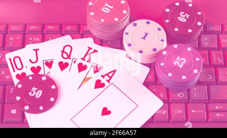 Gaming casino chips and cards on laptop keyboard toned in pink. Stock Photo