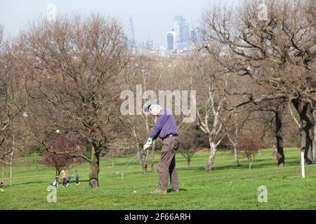 London, UK. March 30 2021: At Dulwich & Sydenham Gold Club, a warm-up on the putting green comes with spectacular views of the London skyline. Warm weather and lockdown easing from coronavirus restrictions now means that outdoor sport is allowed. Credit: Anna Watson/Alamy Live News Stock Photo