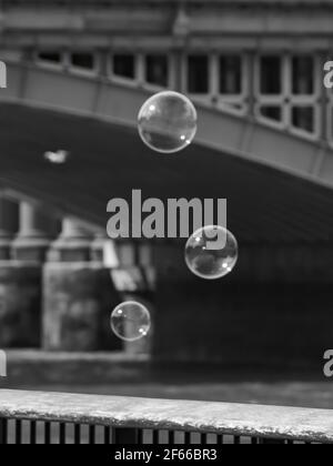 Light, peaceful image of a trio of soap bubbles rising into the summer sky, against a de-focused railway bridge background. Stock Photo