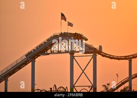 Sunset landscape with people silhouettes riding the Roller coaster at Santa Monica Amusement Park in California, USA. Stock Photo