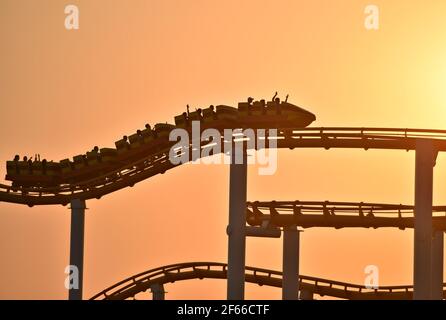 Sunset landscape with people silhouettes riding the Roller coaster at Santa Monica Amusement Park in California, USA. Stock Photo