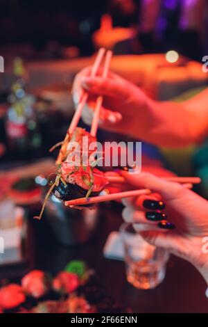 Young couple with chopsticks takes sushi from a plate in a japanese restaurant. Men and women starts eats japanese food. Focus on the seafood plate, c Stock Photo