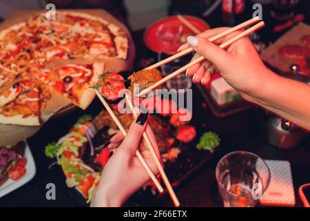 Young couple with chopsticks takes sushi from a plate in a japanese restaurant. Men and women starts eats japanese food. Focus on the seafood plate, c Stock Photo