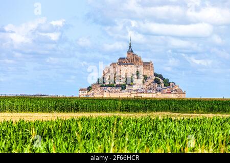View of famous historic Le Mont Saint-Michel tidal island with green corn fields infront