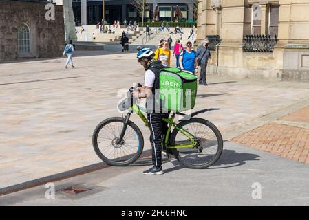 An Uber Eats delivery cyclist checks details on his smart phone in the centre of Birmingham Stock Photo