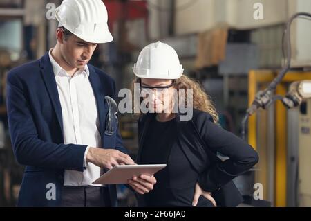 A portrait of an industrial man and woman engineer with tablet in a factory, working. Stock Photo