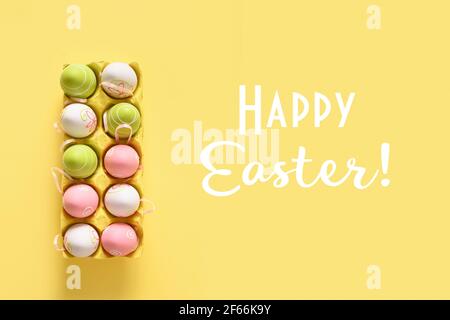 Easter pastel colorful eggs in carton box on yellow background. View from above. Greeting card with text - Happy Easter. Christian custom. Stock Photo