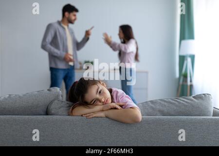 Family conflicts. Sad arab girl sitting alone while her parents arguing on the background Stock Photo