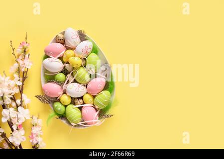 Easter eggs in plate and spring blooming flowers on yellow background with copy space. View from above. Easter greeting card. Stock Photo