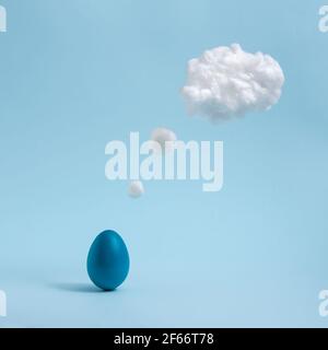Blue Easter egg is thinking. Cotton made cloud like thought balloon. Pastel blue background. Abstract, minimalist concept. Comic book motive. Square Stock Photo