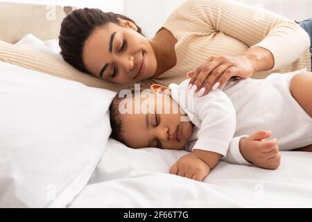 Loving Black Mom Hugging Sleeping Baby Lying In Bed Indoor Stock Photo