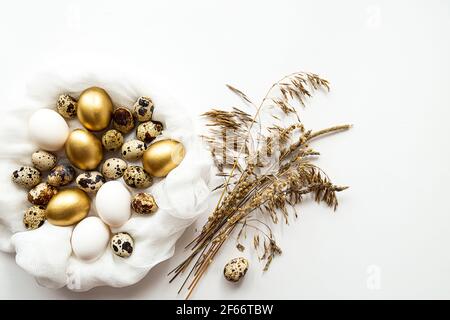 Minimalistic still life, quail eggs, white and gold easter eggs, and dry field spikelets on a white background. Modern Easter holiday concept Stock Photo