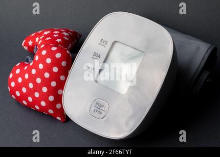 Automatic blood pressure monitor and two soft red hearts on gray background. Medical electronic tonometer closeup. Stock Photo