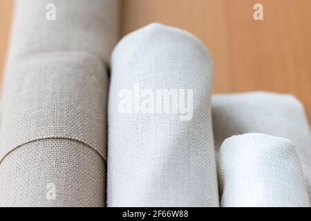Three rolls of natural linen fabric in different colors on a wooden table. Selective focus. Closeup view. Blurred background Stock Photo