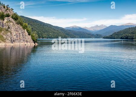 Daylight view to Vidraru lake in Carpathian Mountains. Bright blue sky and green trees. Boat cruising on water. Negative copy space, place for text. T