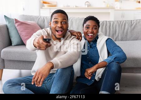 Excited black couple spending weekend together watching tv Stock Photo