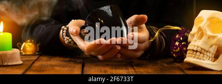 A fortune-teller or oracle with objects for fortune-telling is holding a cup with leftover coffee in her hands, fortune-telling on the coffee grounds. Stock Photo