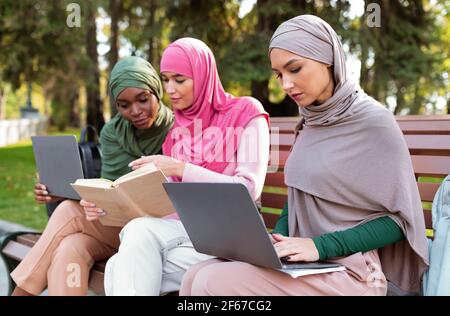Three Islamic Women Learning Using Computers And Reading Books Outdoor Stock Photo