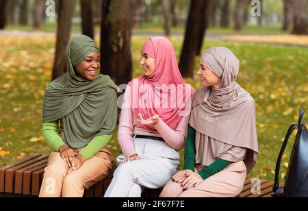 Muslim Young Women Talking Sitting On Bench In Park Outdoors Stock Photo
