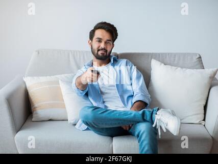 Smiling Young Middle Eastern Guy Watching TV At Home. Stock Photo
