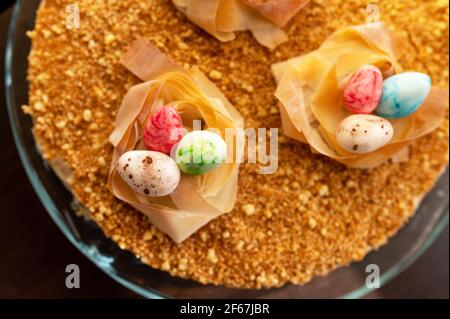Easter cake with yellow mirror glaze, chocolate, spring flowers, quail eggs on dark stone background. Happy Easter celebration, selective focus. Stock Photo
