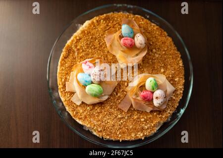 Easter cake with yellow mirror glaze, chocolate, spring flowers, quail eggs on dark stone background. Happy Easter celebration, selective focus. Stock Photo