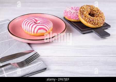 Three sugar-coated donuts lie on a pink ceramic plate and a slate board. Serving with cutlery and linen napkin. Stock Photo