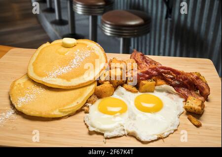 Diner style slam breakfast.  Two eggs sunny side up, bacon, hash browns, and two pancakes. Stock Photo