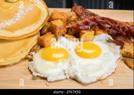 Diner style slam breakfast.  Two eggs sunny side up, bacon, hash browns, and two pancakes. Stock Photo