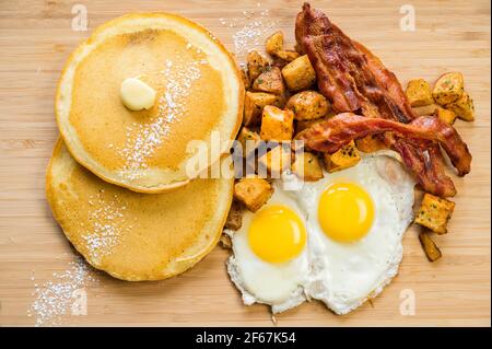 Diner style slam breakfast.  Two eggs sunny side up, bacon, hash browns, and two pancakes. Stock Photo