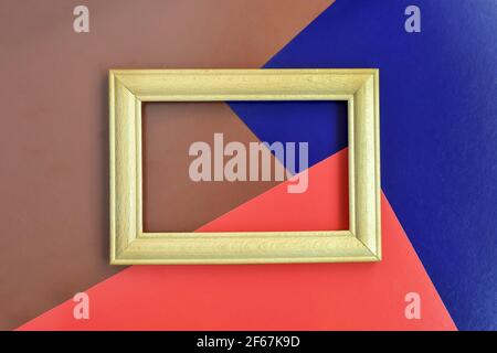 Empty wooden frame made of beech on multi-colored abstract paper background. Red, blue, brown. Place for photo. Horizontal placement. Mockup. Close-up Stock Photo