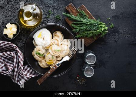 Pelmeni, meat stuffed boiled dumplings served with butter and sour cream. Black concrete background, top view Stock Photo