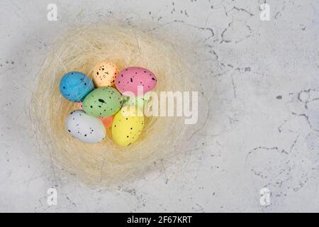 Multicolored Easter eggs in a nest on a white concrete background. Stock Photo
