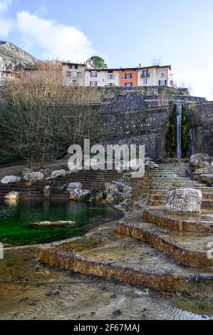 Wide stone stairs leading around water surface to waterfall. Row of houses above stone wall. La cascade monumental, Pont-en-Royans, France. Stock Photo