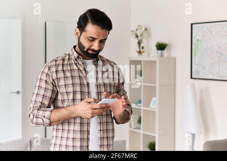 Young indian man holding smartphone using cell phone at home. Stock Photo